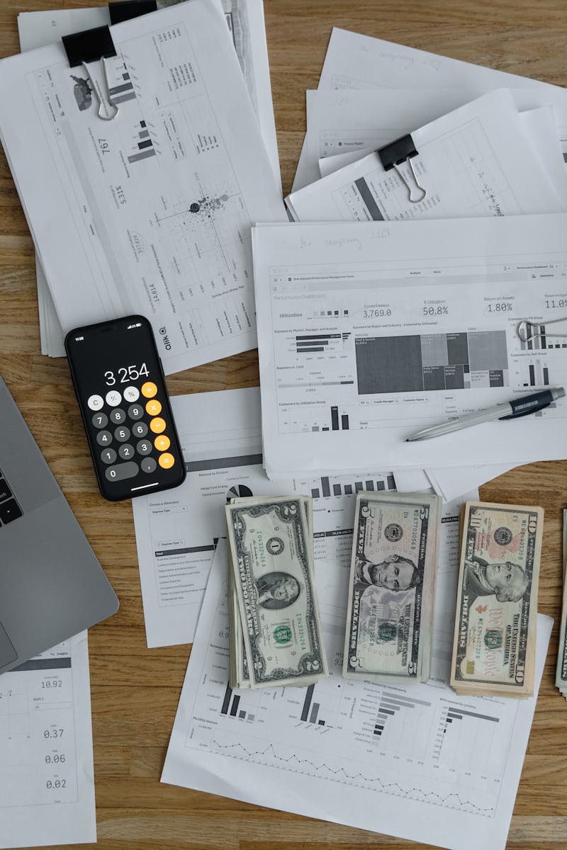 Overhead view of financial documents, cash, and technology on a wooden desk.